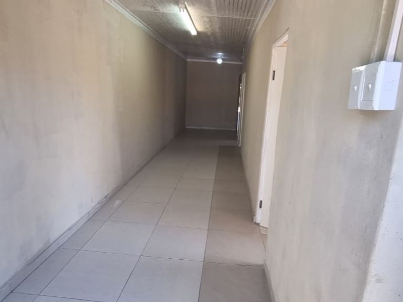 A long, empty hallway featuring tiled flooring, surface-mounted electrical conduits, and basic ceiling lighting, requiring cosmetic updates to improve the overall finish.