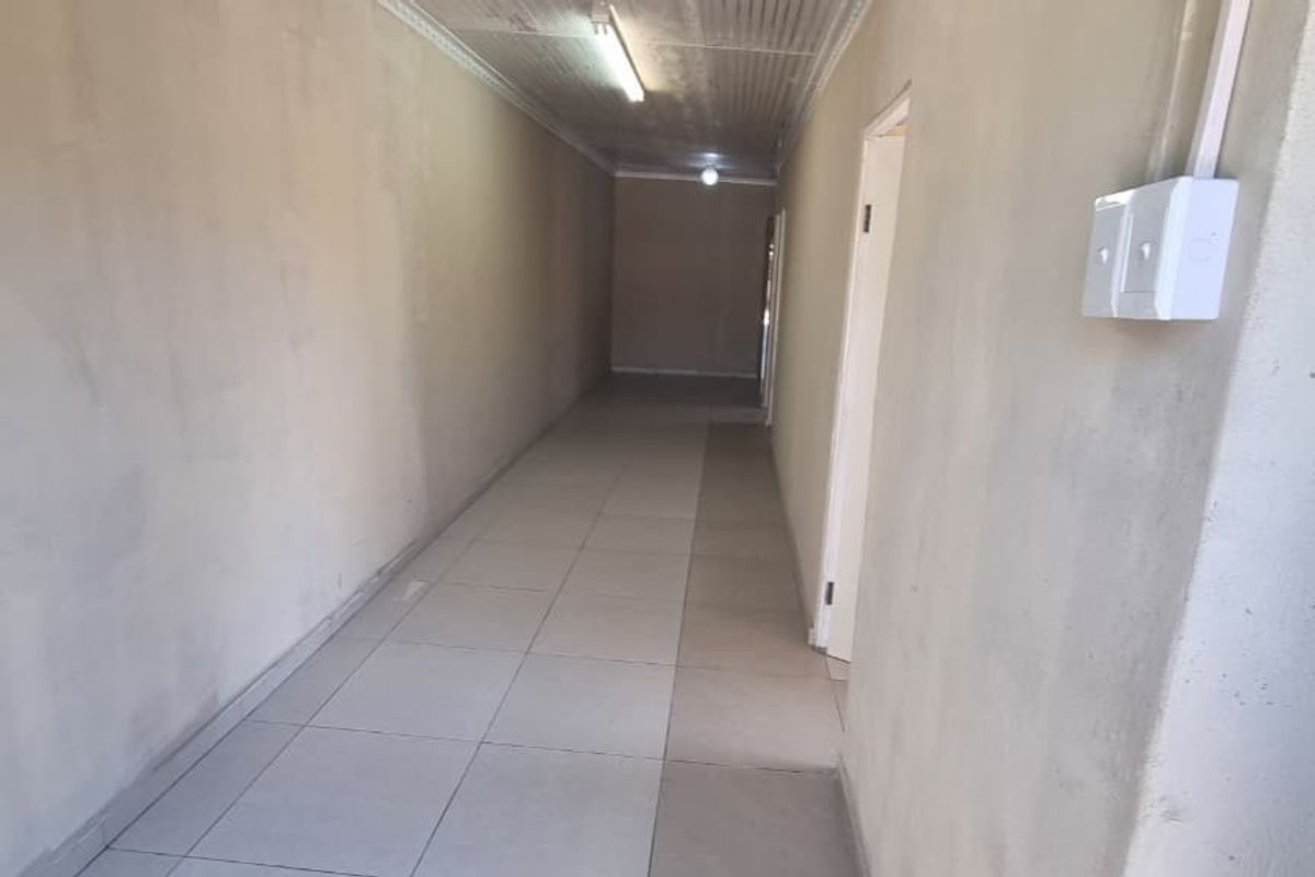 A long, empty hallway featuring tiled flooring, surface-mounted electrical conduits, and basic ceiling lighting, requiring cosmetic updates to improve the overall finish.