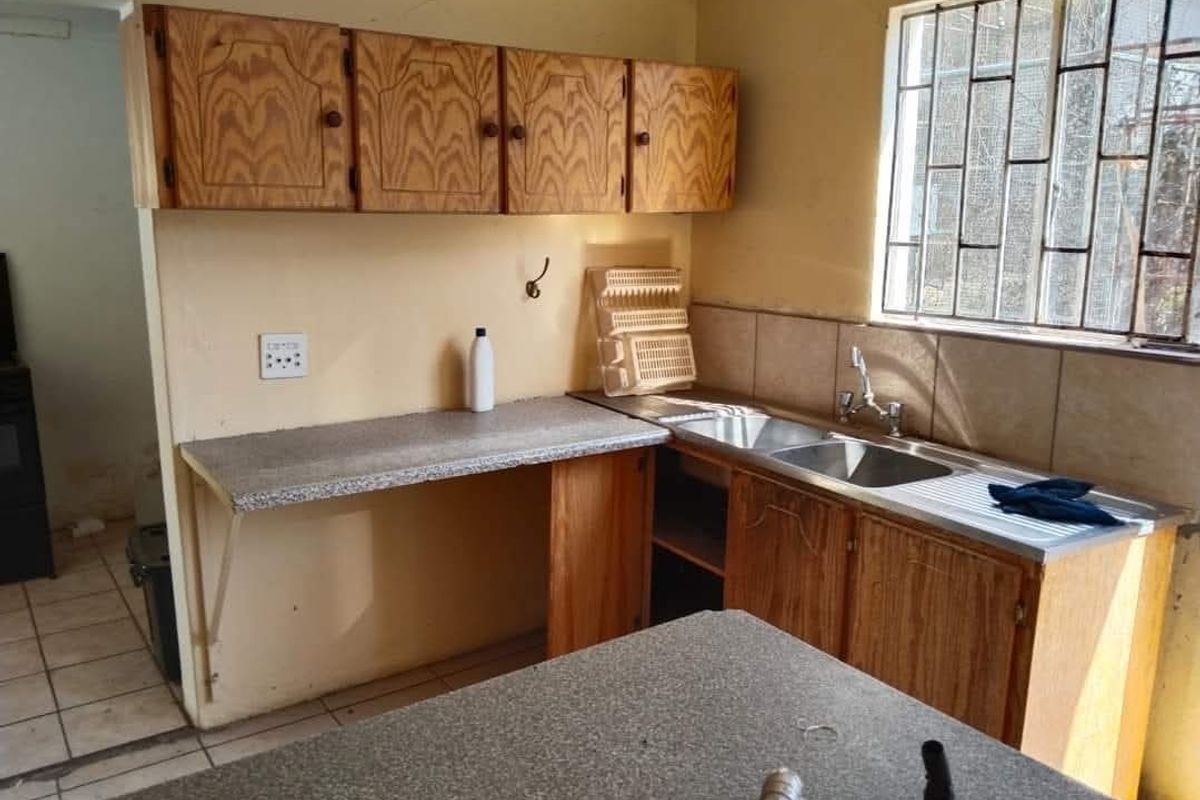 A dated kitchen featuring wooden cabinetry, laminate countertops, and a double stainless steel sink, requiring cosmetic updates to modernize the space.