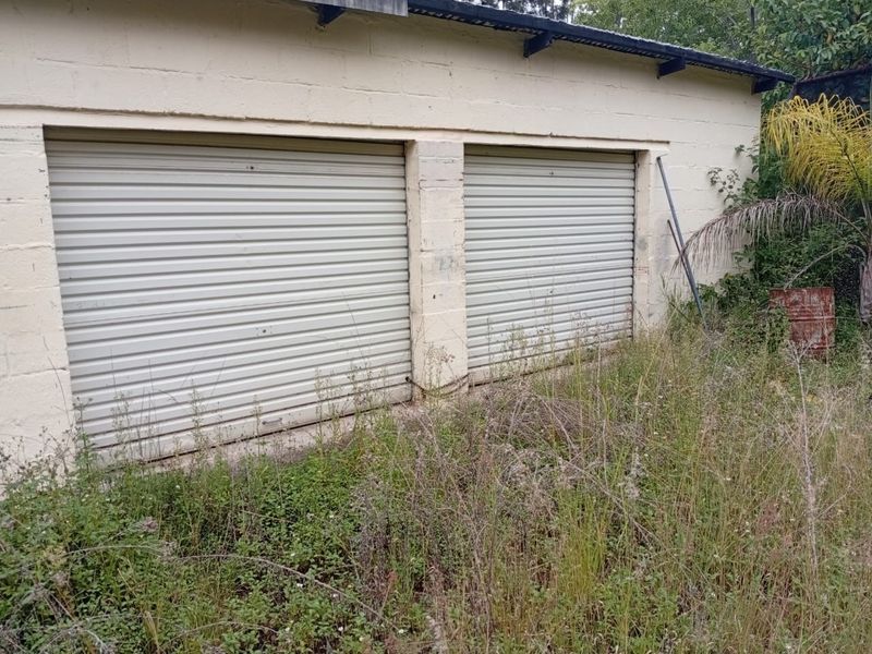 A detached double garage featuring roller doors and concrete block construction, currently surrounded by overgrown vegetation.