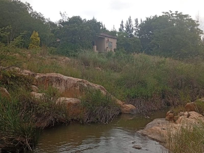A scenic view of a natural stream and rock formations on the farm property, with the main dwelling visible in the background.
