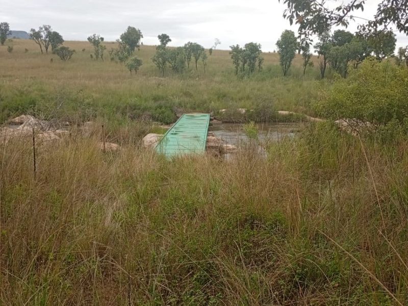 A view of the farm landscape featuring a small green footbridge crossing a natural stream amidst open grassland.