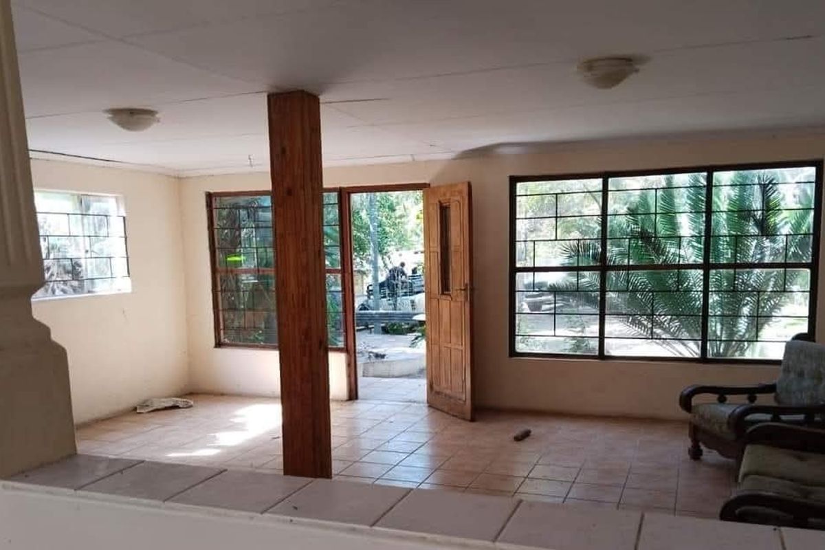 Spacious living area featuring tiled flooring, a central timber support column, and large windows with security bars, offering direct access to the exterior.