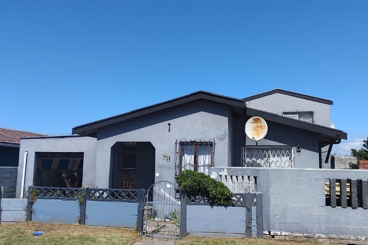 Front elevation of a single-story house featuring a grey painted facade, security gates, and a front boundary wall with a paved walkway.