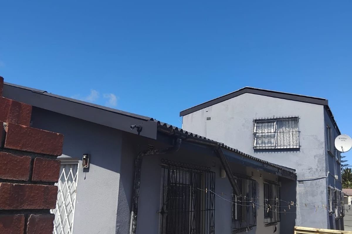 Rear exterior view of the property featuring grey painted walls, security bars on windows, and a paved outdoor area.