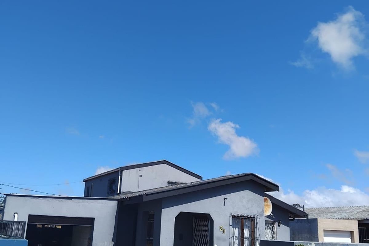 Front elevation of a single-story house featuring a paved driveway, garage, and secure boundary wall with metal gates.