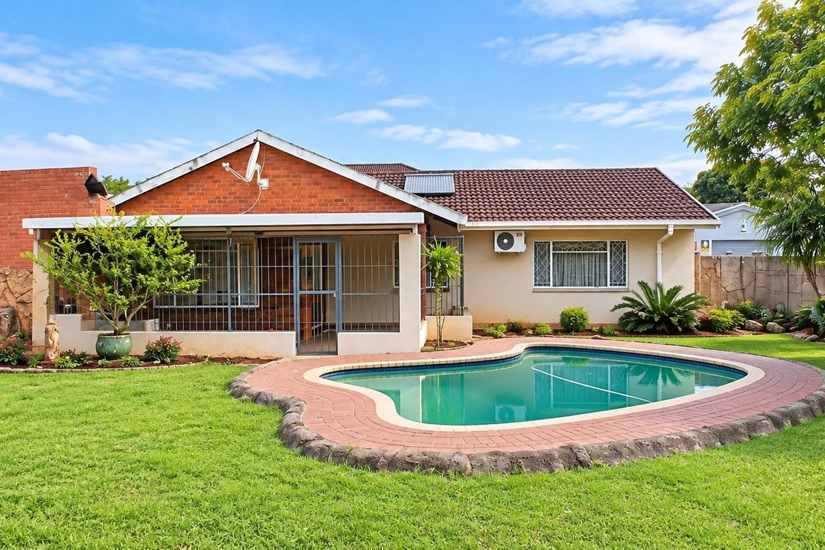 Rear view of the house featuring a swimming pool, brick-paved surround, covered patio area, and well-maintained garden.