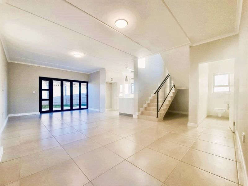 Spacious open-plan living area featuring neutral tiled flooring, a modern staircase, and large black-framed sliding doors leading to the exterior.