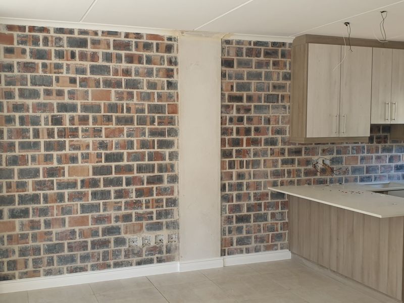 Open plan living and kitchen area featuring an exposed brick wall, built-in fireplace, and modern cabinetry. The space is currently undergoing final finishing touches.