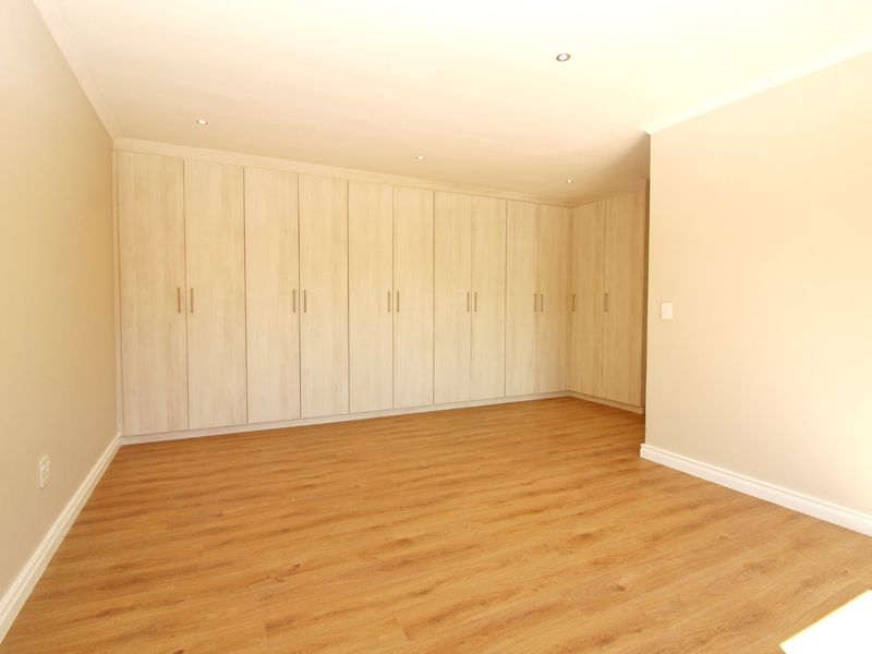 A bright, empty bedroom featuring extensive floor-to-ceiling built-in cupboards, modern laminate flooring, and recessed ceiling lighting.