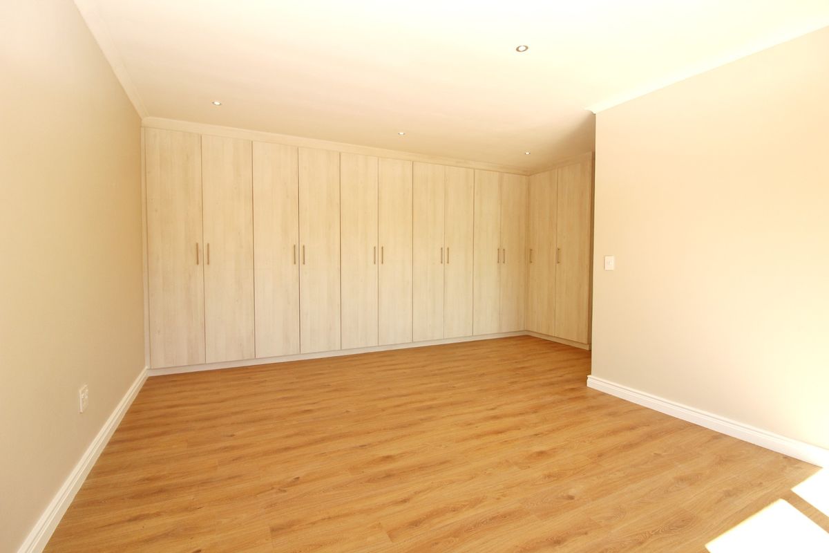A bright, empty bedroom featuring extensive floor-to-ceiling built-in cupboards, modern laminate flooring, and recessed ceiling lighting.