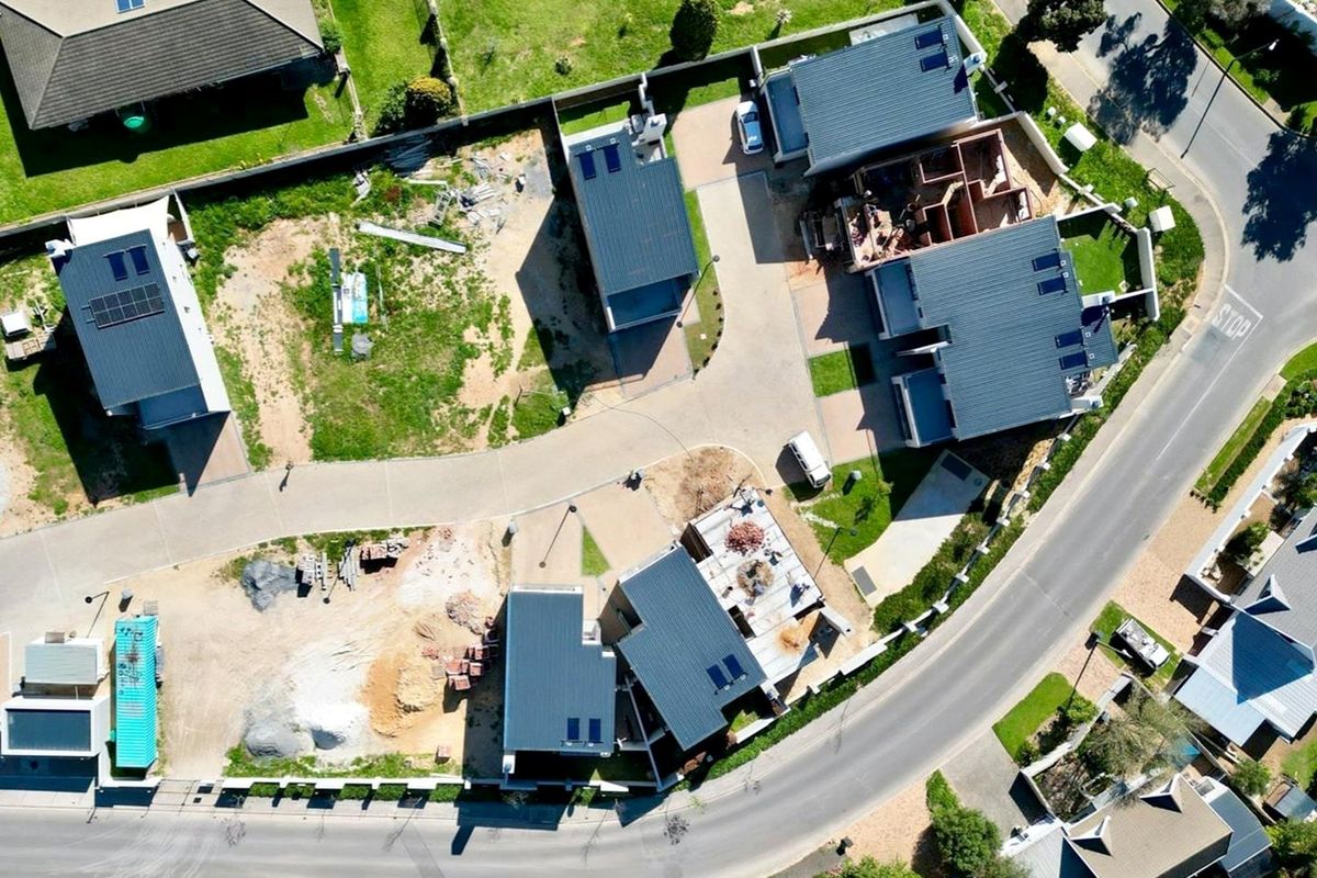 Aerial view of a residential development site showing multiple houses in various stages of construction with paved access roads and installed solar panels.