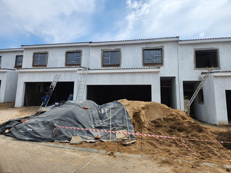 A front view of a residential property currently under construction, featuring an unfinished facade, garage openings, and ongoing site work.