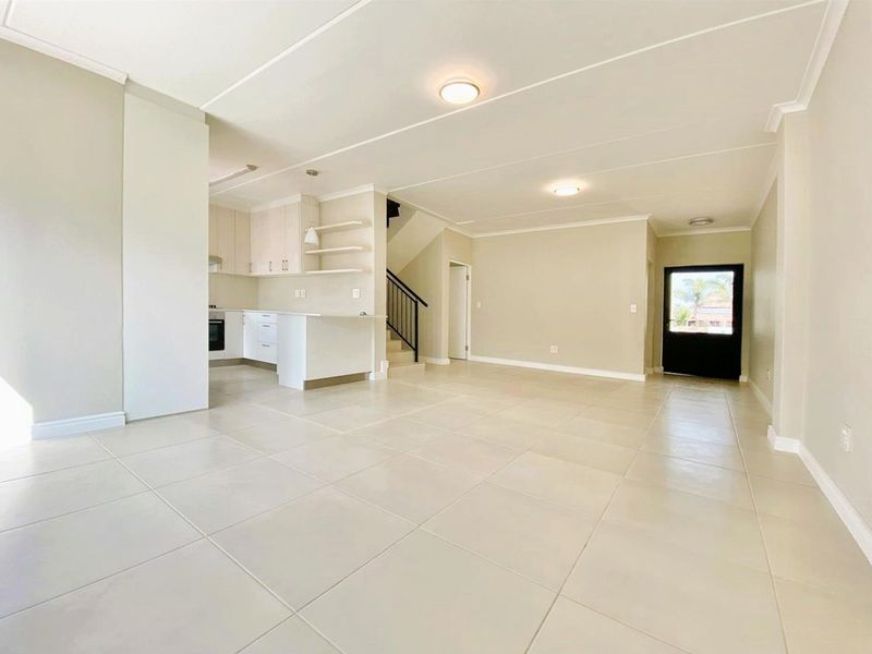 Spacious open-plan living area featuring neutral tiled flooring, a modern kitchen with built-in cabinetry, and a staircase leading to the upper level.
