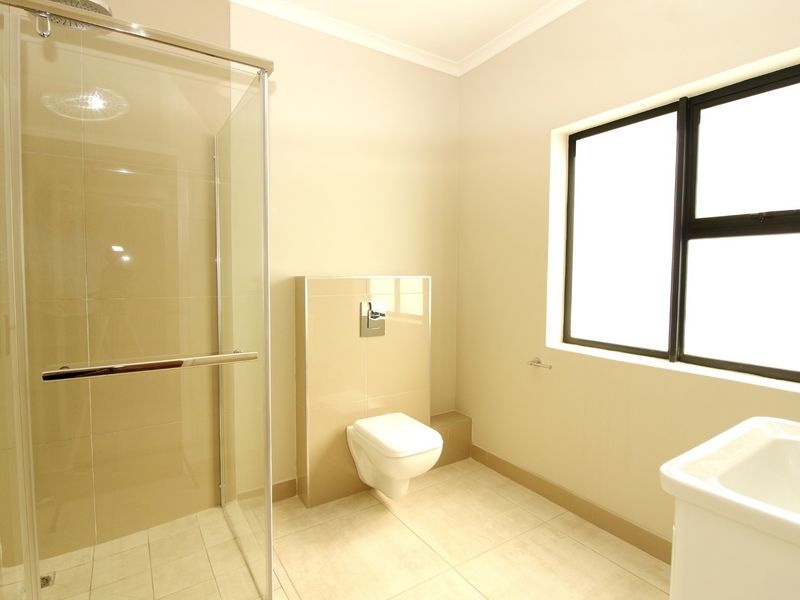 A clean, modern bathroom featuring a glass-enclosed shower, wall-mounted toilet with concealed cistern, and neutral tiled finishes.