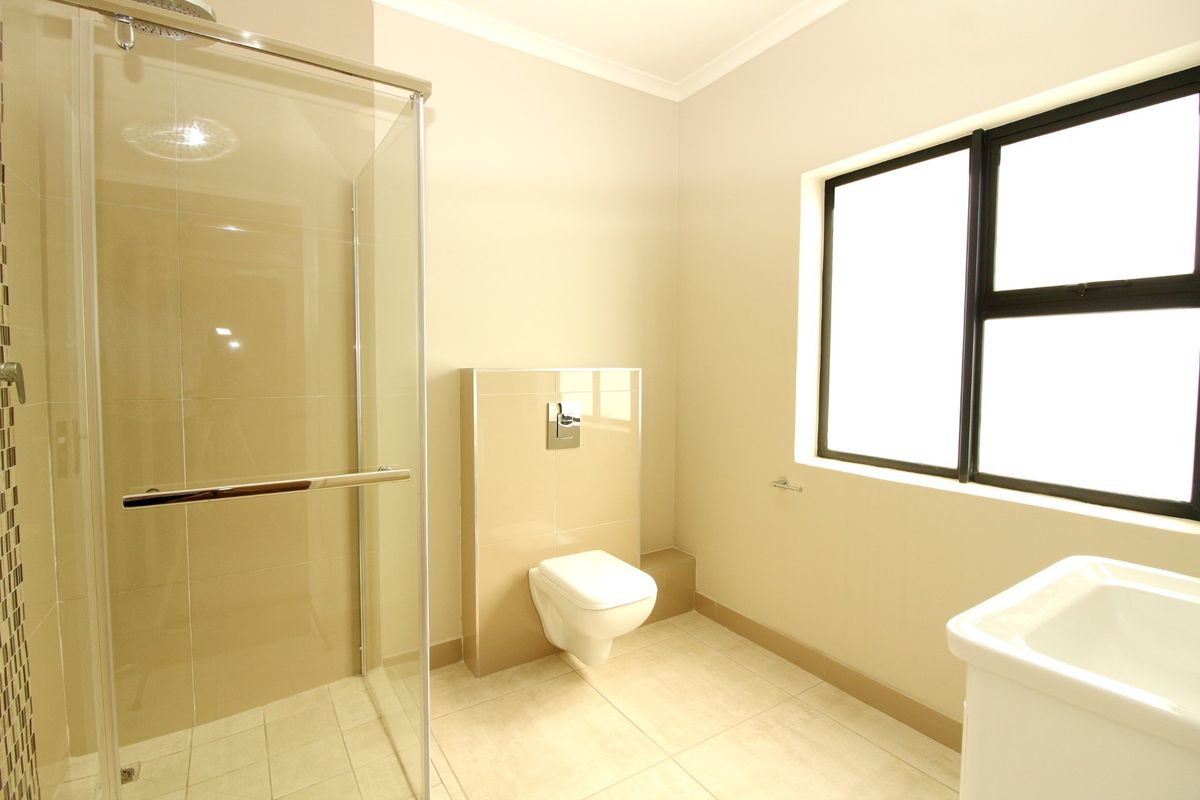 A clean, modern bathroom featuring a glass-enclosed shower, wall-mounted toilet with concealed cistern, and neutral tiled finishes.