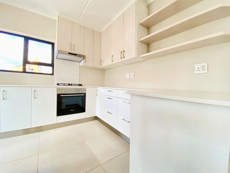 Modern kitchen featuring sleek white cabinetry, integrated oven and hob, stone countertops, and neutral tiled flooring in a clean, minimalist design.