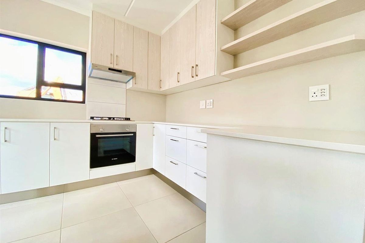 Modern kitchen featuring sleek white cabinetry, integrated oven and hob, stone countertops, and neutral tiled flooring in a clean, minimalist design.