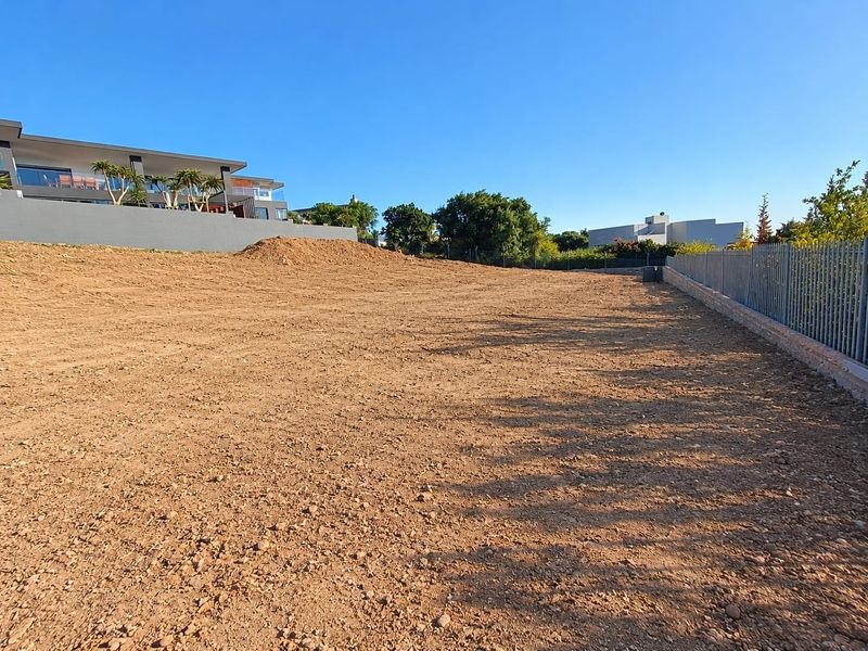 A vacant residential plot of land featuring cleared earth, perimeter fencing, and a retaining wall, ready for development.