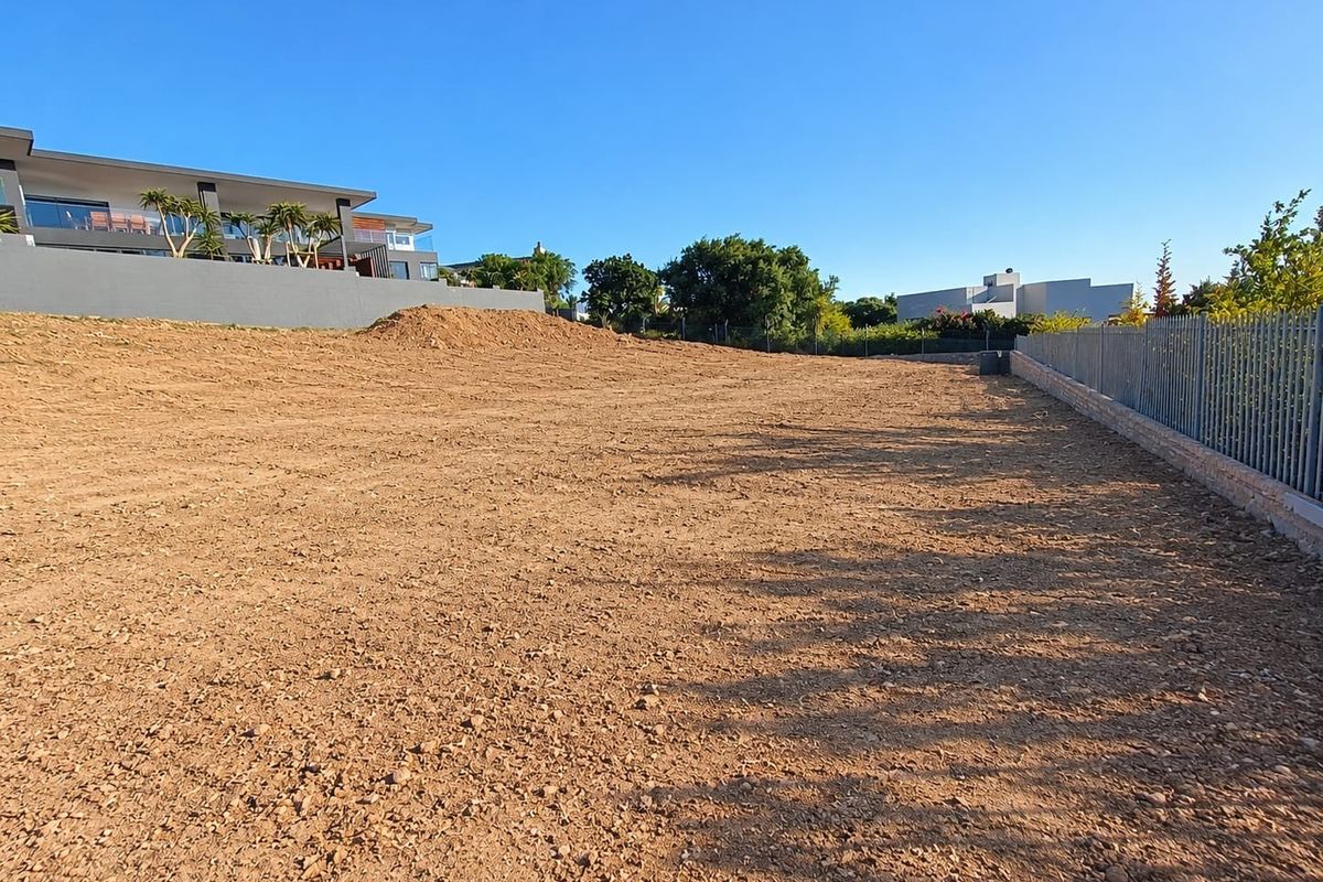 A vacant residential plot of land featuring cleared earth, perimeter fencing, and a retaining wall, ready for development.