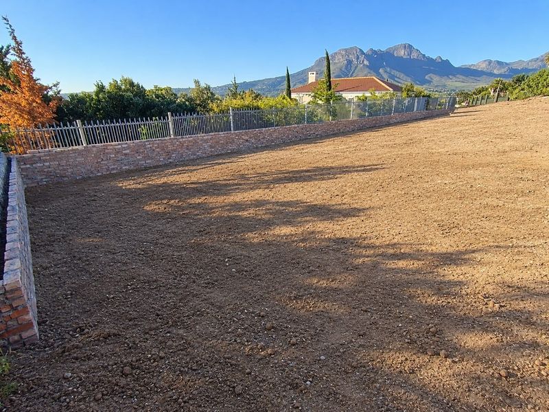 A cleared, level residential plot featuring a brick boundary wall with metal fencing, offering scenic mountain views.