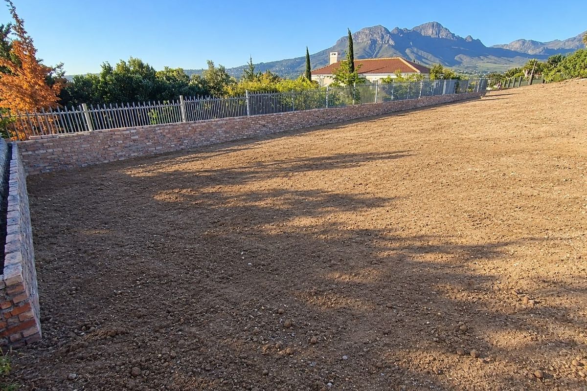 A cleared, level residential plot featuring a brick boundary wall with metal fencing, offering scenic mountain views.