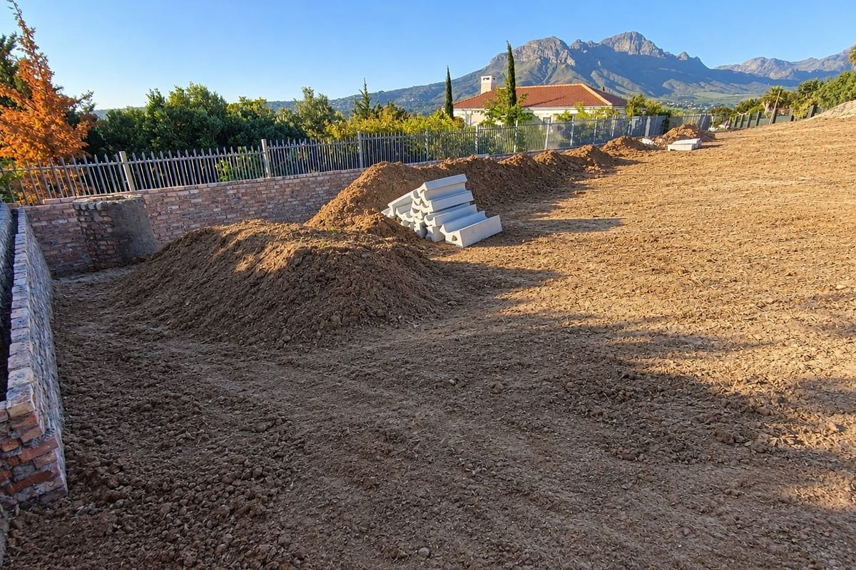 Vacant residential land featuring a brick retaining wall, metal fencing, and mountain views, currently undergoing site preparation.