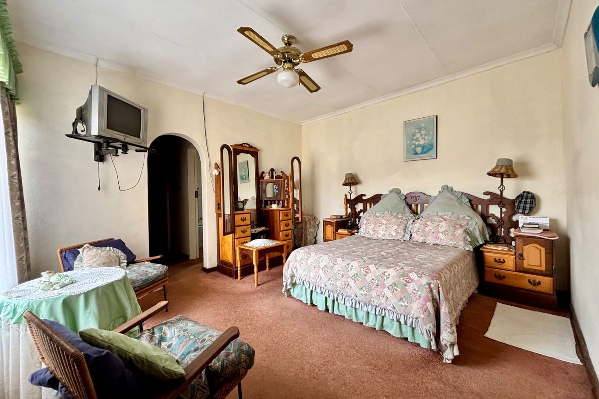 A spacious bedroom featuring a ceiling fan and an arched doorway, with dated finishes and carpet flooring throughout.