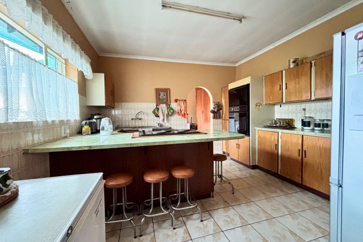 A dated kitchen featuring original wood cabinetry, laminate countertops, and ceramic tile flooring, offering significant potential for a modern renovation.