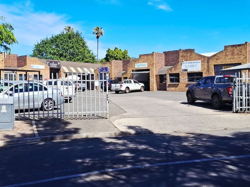 Front view of an industrial park complex featuring brick facade buildings, paved driveway access, and secure perimeter fencing.