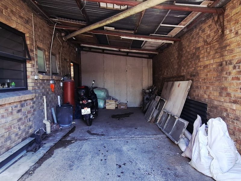 A functional industrial garage space featuring exposed brick walls, a corrugated metal roof, and concrete flooring, suitable for storage or workshop use.