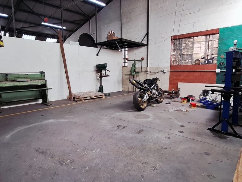 Industrial utility space featuring exposed steel roof trusses, concrete flooring, and a spiral staircase, suitable for workshop or storage use.