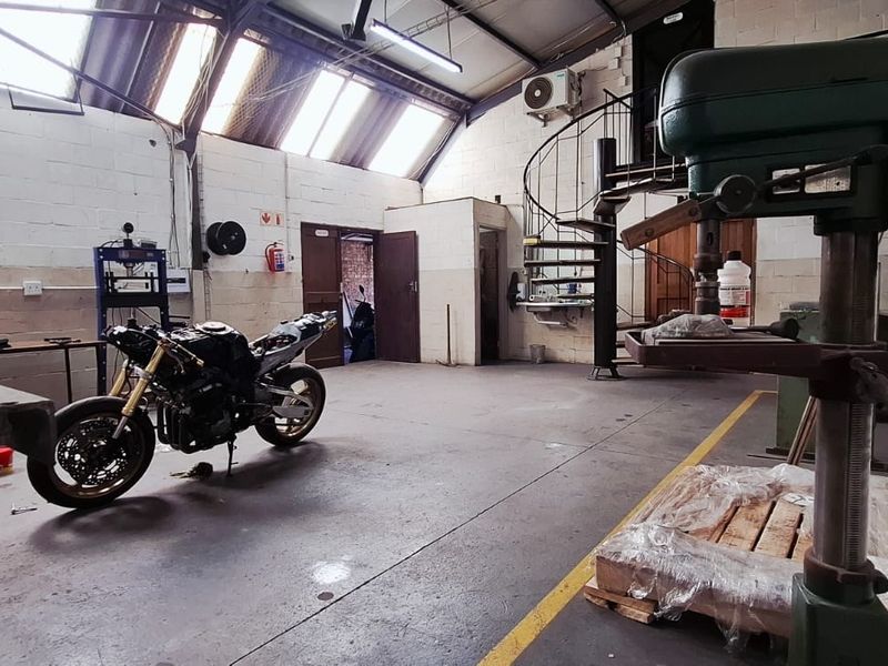 Spacious industrial utility area featuring high ceilings with skylights, concrete flooring, a spiral staircase, and wall-mounted air conditioning.