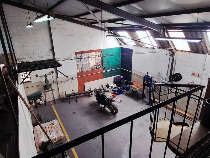 Spacious industrial utility area featuring high ceilings with exposed steel trusses, skylights, concrete flooring, and a metal staircase leading to an upper level.
