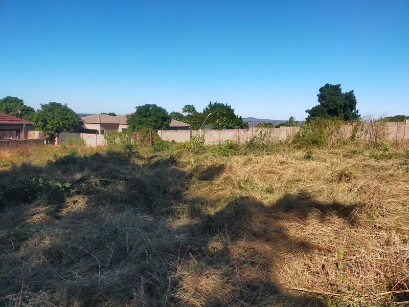 A view of a vacant residential plot featuring cleared grass and a perimeter boundary wall.
