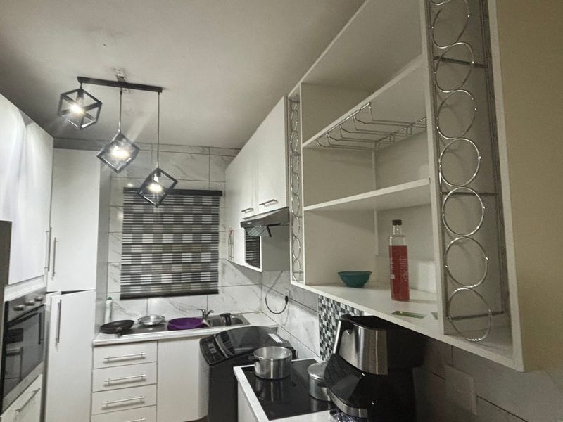A modern kitchen featuring white cabinetry, marble-look wall tiles, built-in oven, hob, extractor fan, and stylish geometric pendant lighting.