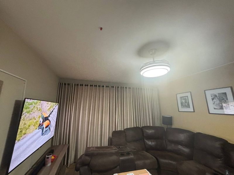 A living room featuring a ceiling fan with integrated lighting and full-length curtains, providing a functional and comfortable space.
