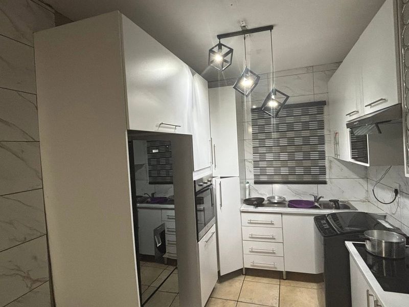A compact, modern kitchen featuring white built-in cabinetry, marble-look wall tiling, integrated oven, and contemporary pendant lighting.