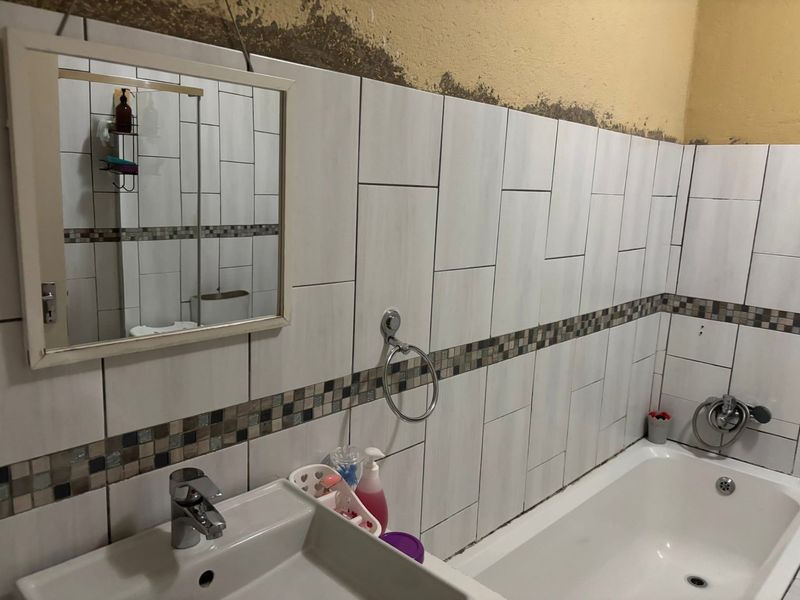 Bathroom featuring a bathtub and basin with tiled walls. The upper wall area requires finishing and painting to complete the space.