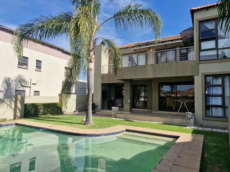 Rear view of the property featuring a swimming pool, a covered patio with a built-in braai, and an upper-level balcony.