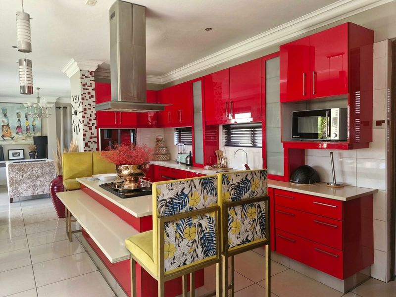 Modern kitchen featuring high-gloss red cabinetry, stone countertops, a central island with integrated hob, and a stainless steel extractor fan.