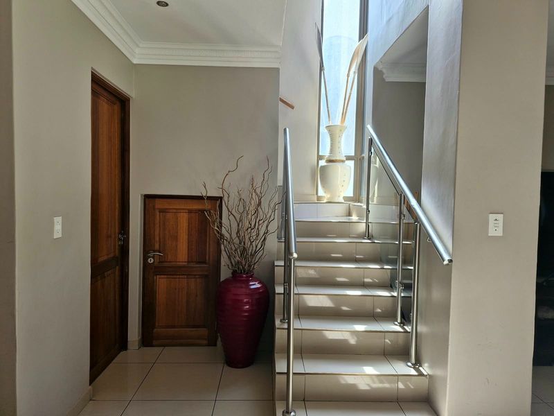 A bright entrance hall featuring tiled flooring, a staircase with a modern stainless steel and glass balustrade, and classic wooden doors.