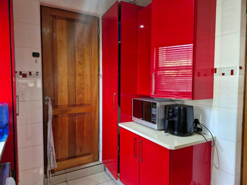 A kitchen area featuring vibrant high-gloss red cabinetry, tiled wall finishes, and a solid wood door, providing a bold and functional storage space.
