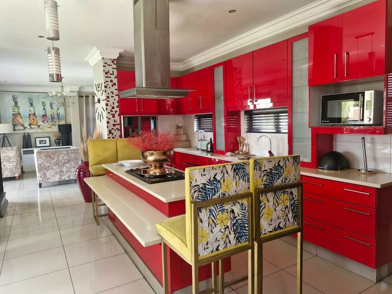 Modern open-plan kitchen featuring high-gloss red cabinetry, stone countertops, and a central island with integrated hob, seamlessly flowing into the adjacent living area.