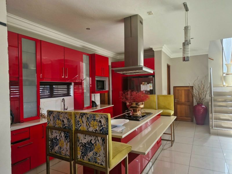 Modern kitchen featuring high-gloss red cabinetry, a central island with integrated cooktop, stainless steel extractor fan, and tiled flooring.