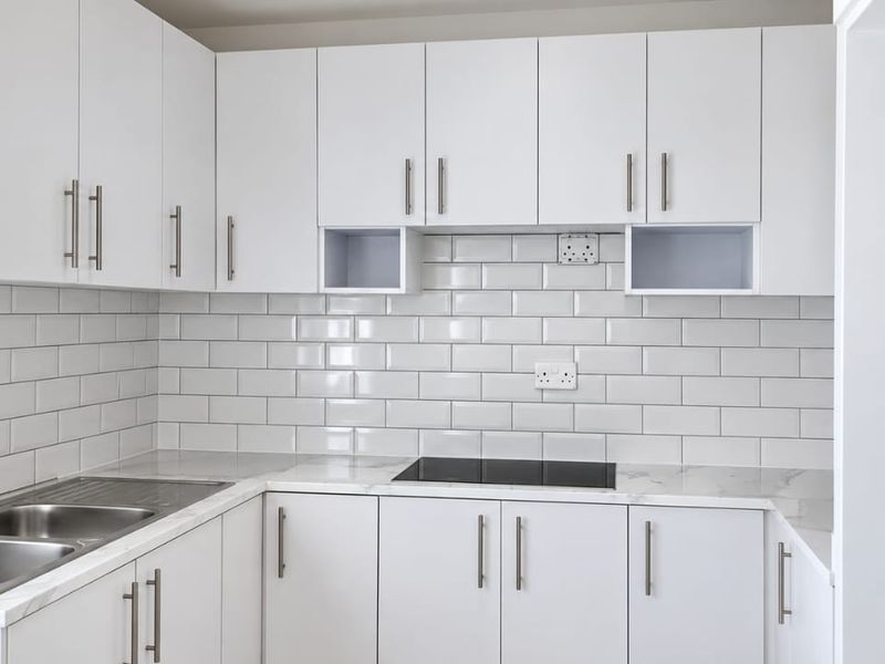 A modern, clean kitchen featuring white cabinetry, subway tile backsplash, marble-look countertops, and a built-in electric hob with a stainless steel sink.
