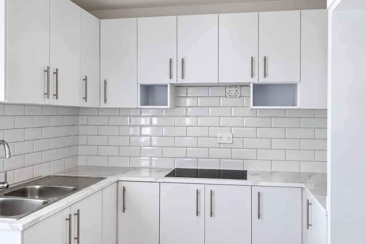 A modern, clean kitchen featuring white cabinetry, subway tile backsplash, marble-look countertops, and a built-in electric hob with a stainless steel sink.