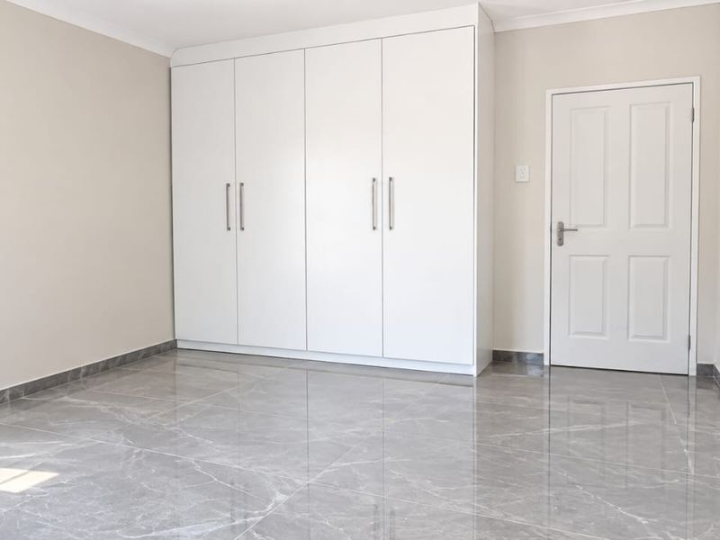 A bright, empty bedroom featuring modern grey marble-look floor tiles, built-in white cupboards, and a clean, neutral aesthetic.