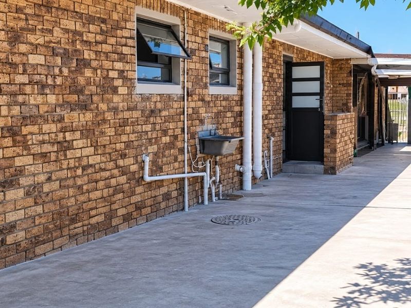 Rear exterior view of the apartment featuring a face brick facade, concrete driveway, utility sink, and secure boundary walling.