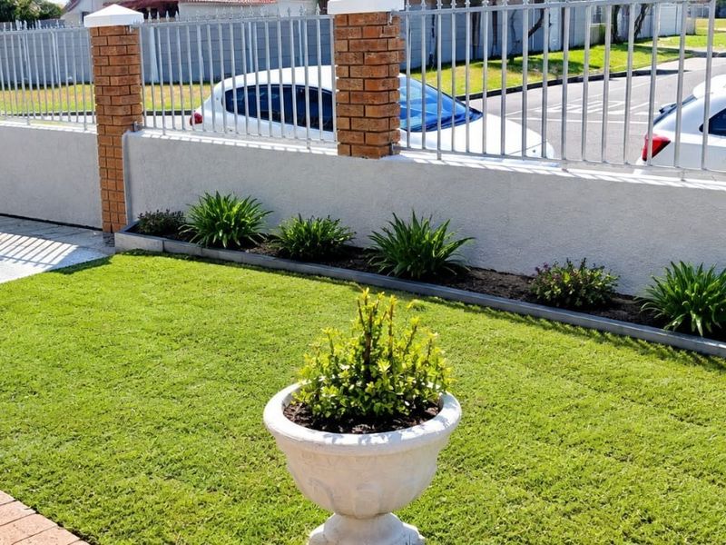 A well-maintained front exterior featuring a brick and plaster boundary wall with metal security fencing, a paved driveway, and a neat garden area.